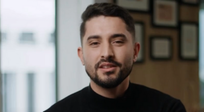 Ahmed, a PhD student in Predictive Maintenance, smiling in a professional office setting during a testimonial about his thesis research.