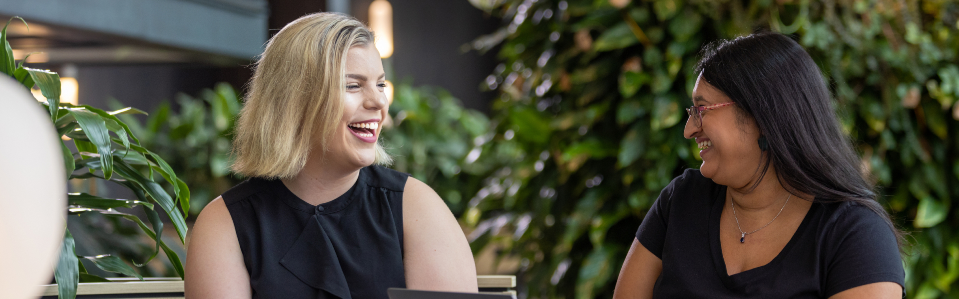 Two women laughing in front of green wall